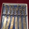 Angled view of six vintage butter knives with tarnished blades and dragon grips