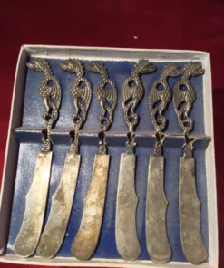 Angled view of six vintage butter knives with tarnished blades and dragon grips