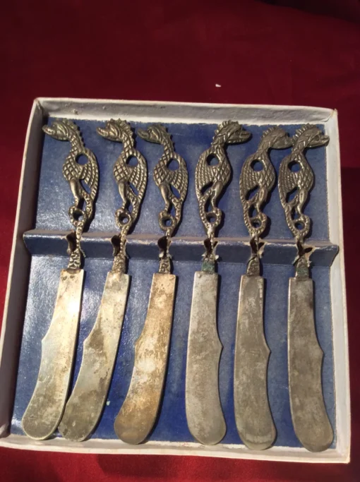 Angled view of six vintage butter knives with tarnished blades and dragon grips