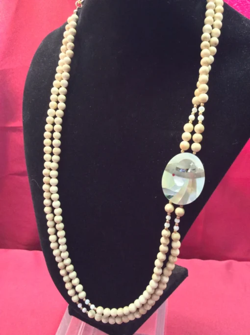 Vintage beaded necklace with double strands and shell inlay pendant on display bust.